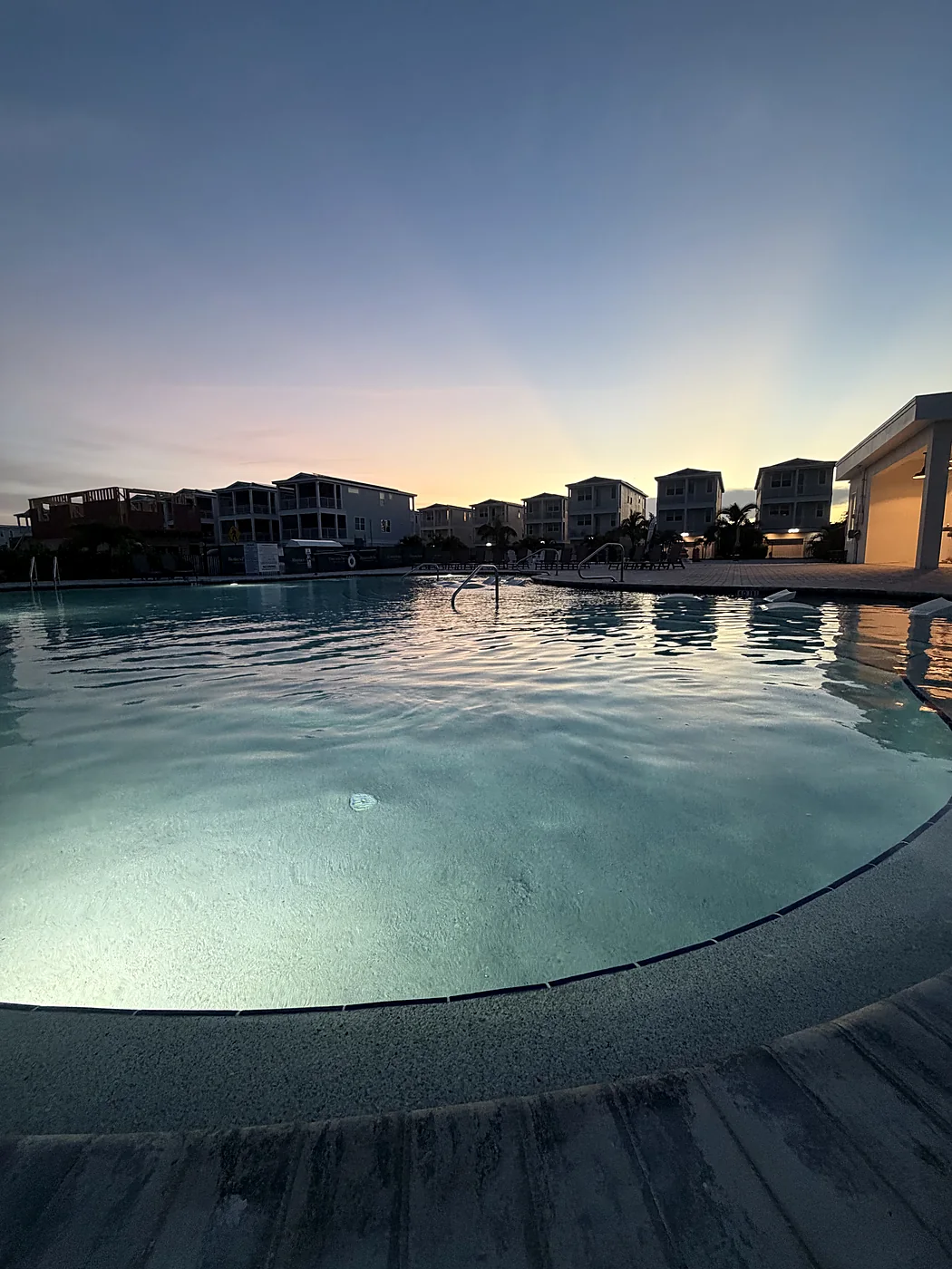 Community pool lit from below at dusk, with townhomes and a sunset behind it