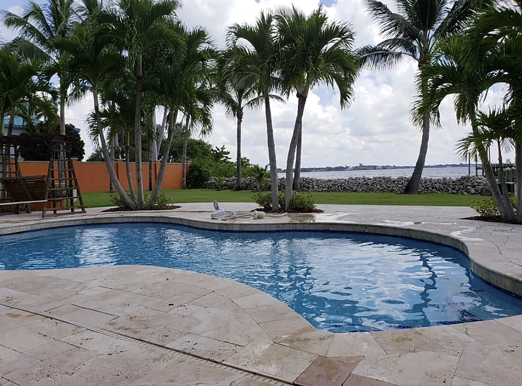 Clear blue pool on a travertine deck with palm trees and a bay view
